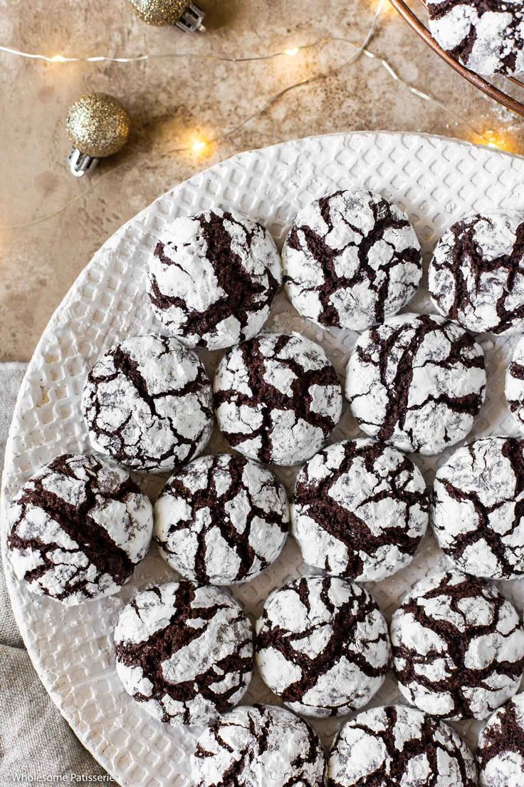 the best chocolate crinkle cookies on a white plate with christmas lights in the background