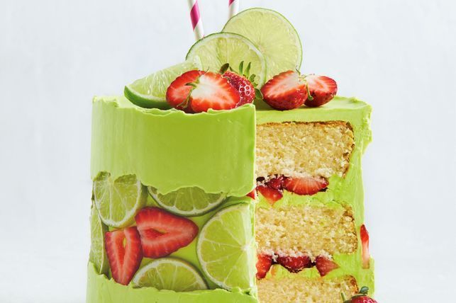 a green cake with strawberries and limes on it is cut in half to show the inside