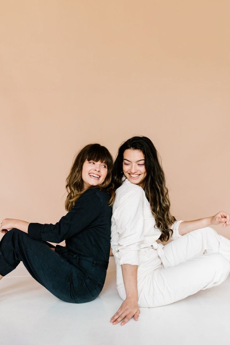 two young women sitting on the ground posing for a photo with their arms around each other