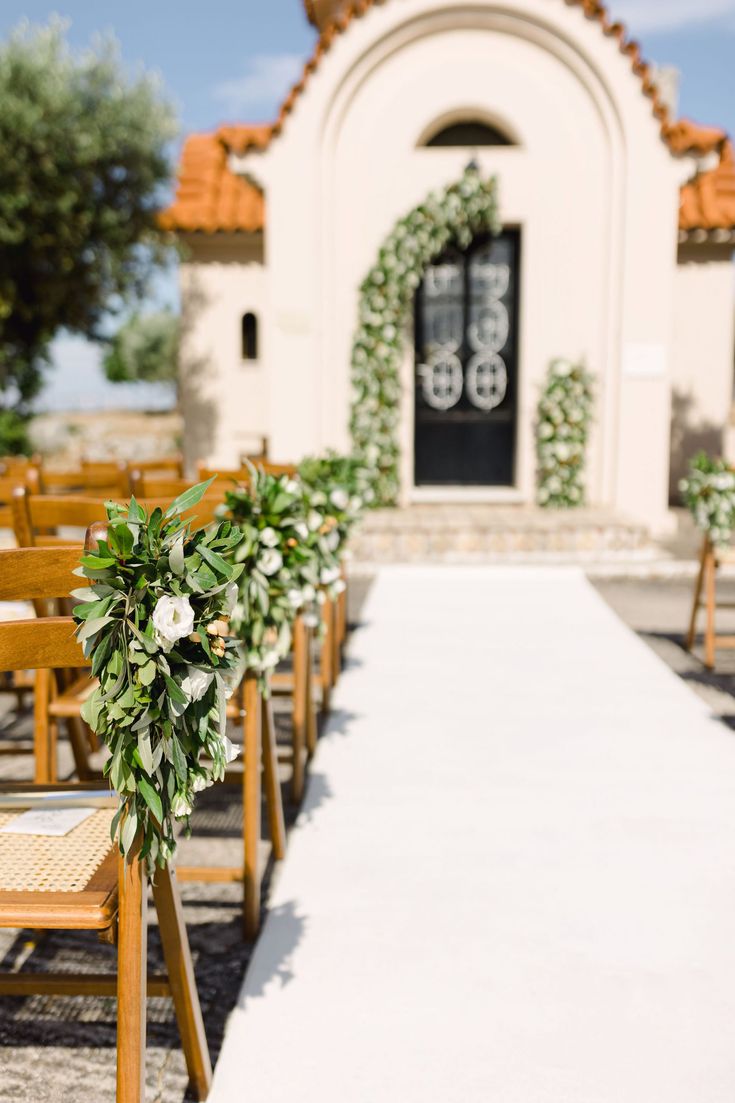 an outdoor ceremony with wooden chairs and greenery in front of a church door on a sunny day