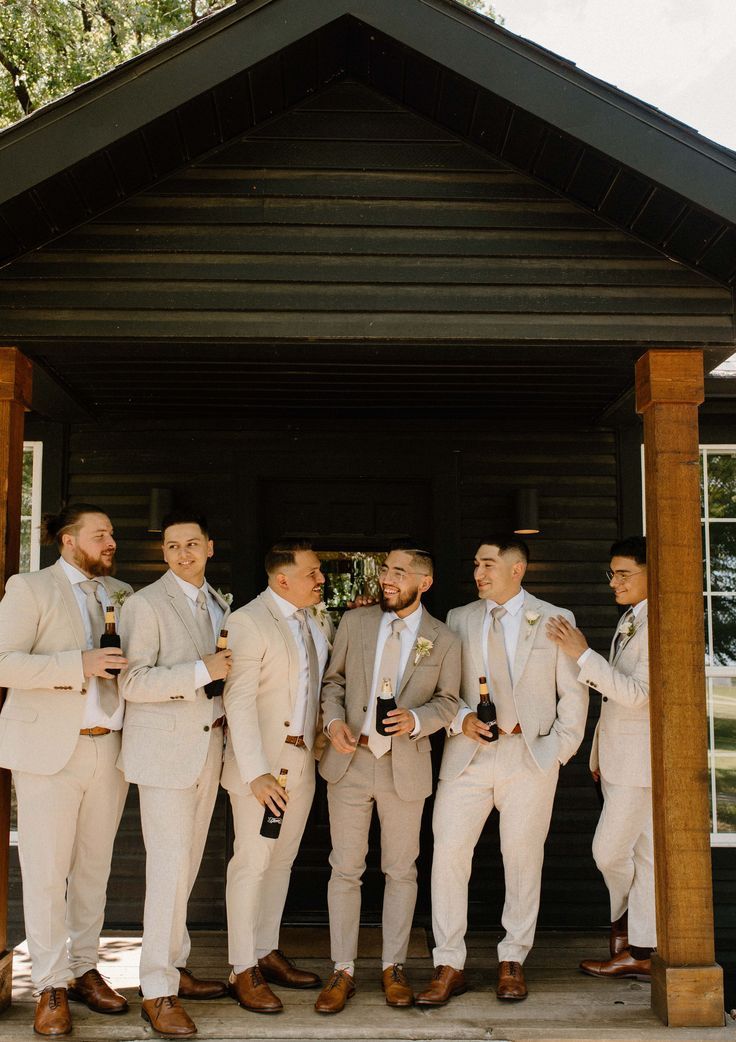 a group of men standing next to each other in front of a wooden structure holding wine glasses