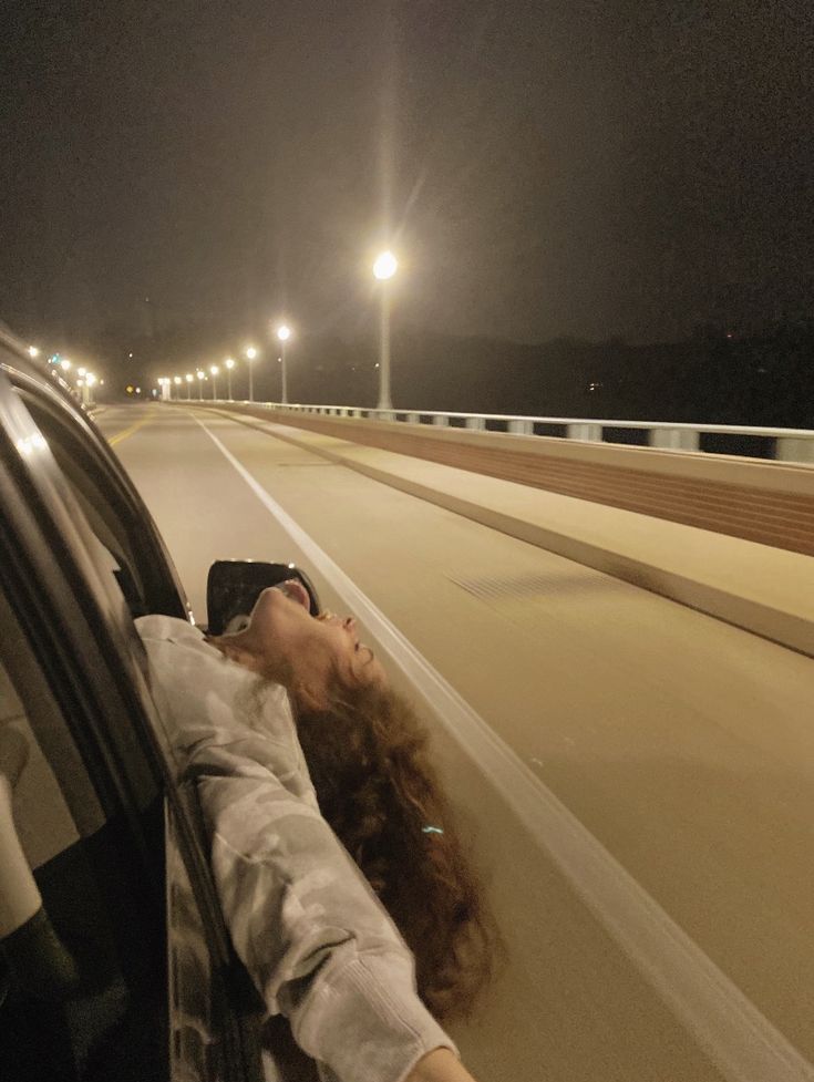 a woman laying her head out the window of a car on a highway at night