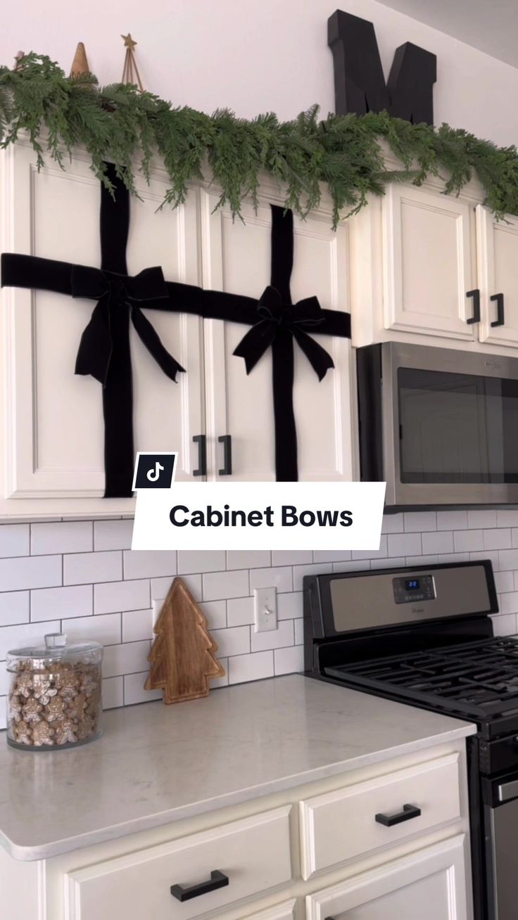 a kitchen with white cabinets and black bows on the wall above the stove top is decorated for christmas