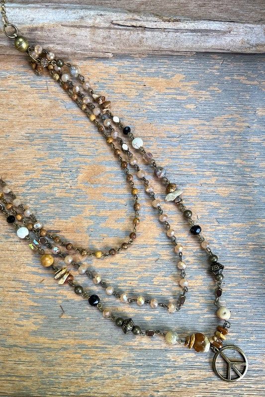 Three layer earth tone beaded necklace. Peace charm. Handmade Brown Necklaces For Layering, Adjustable Spiritual Necklaces For Layering, Spiritual Gemstone Beads Necklace For Layering, Spiritual Brown Beaded Chain Necklaces, Spiritual Multi-strand Beaded Long Necklace, Spiritual Round Beads Necklaces For Layering, Everyday Bohemian Crystal Necklaces With Gemstone Beads, Bohemian Long Necklace With Natural Stones For Layering, Gold Jewelry With Colorful Beads For Layering