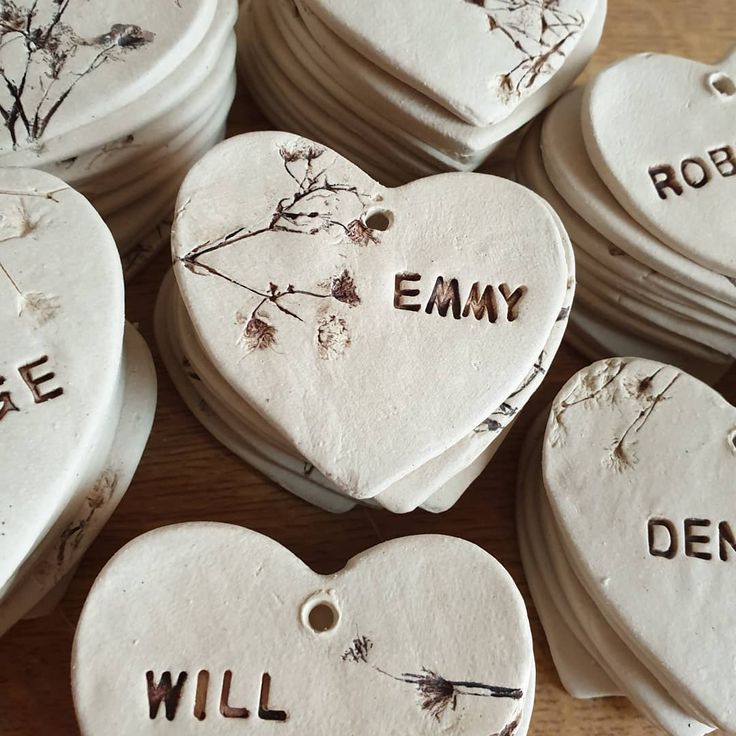 white ceramic heart ornaments with words written on them and dried flowers in the middle, arranged on a wooden surface