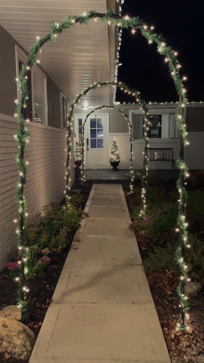 an arch covered in christmas lights on the side of a house next to a sidewalk