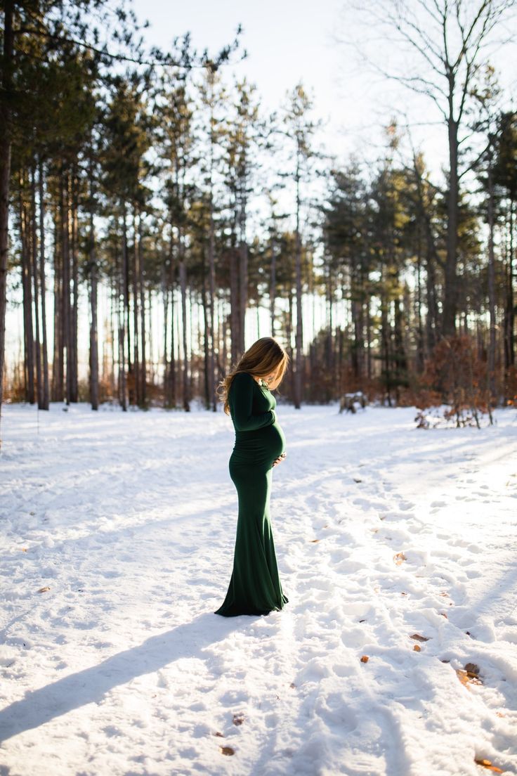 a pregnant woman standing in the snow with her hands on her belly, looking down