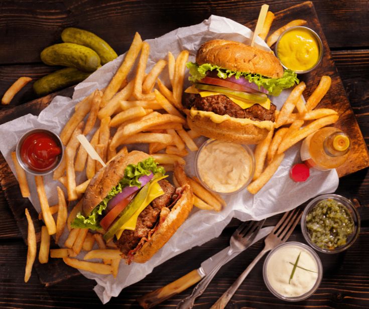 two hamburgers with fries and pickles on a wooden table next to condiments