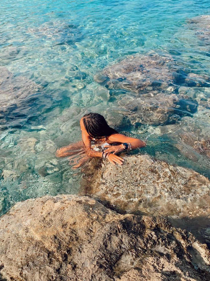 a woman laying on top of a large rock in the ocean next to some rocks