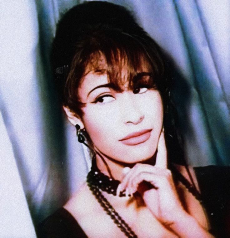 a woman posing for the camera with her hand on her chin and wearing a black dress