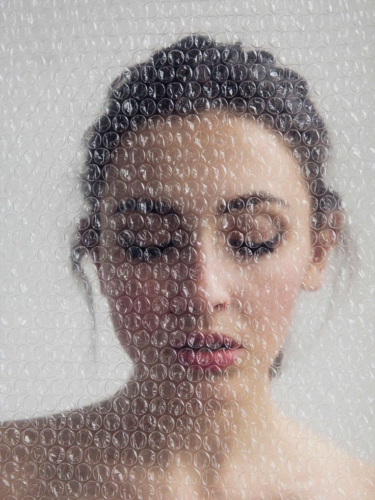 a woman with her eyes closed looking at the camera through a window covered in bubbles