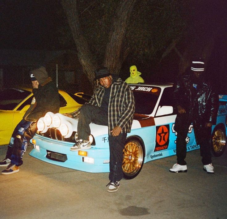 two men sitting on the hood of a race car with another man standing next to it