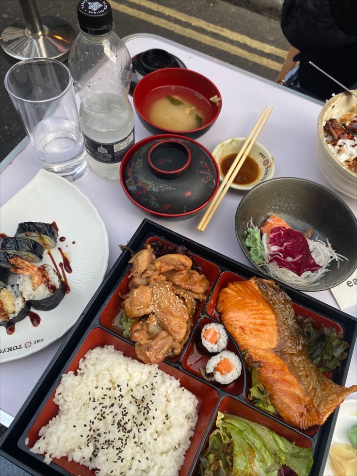 an assortment of sushi and other foods on a table with water, wine glasses, and chopsticks