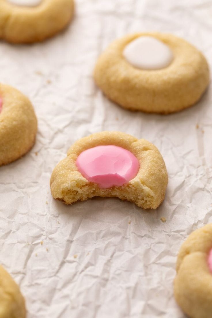 some cookies with pink frosting and white icing are on a sheet of wax paper