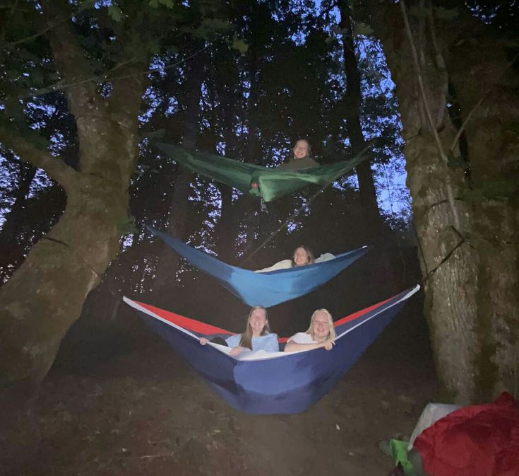 three people laying in hammocks on the ground at night with trees around them