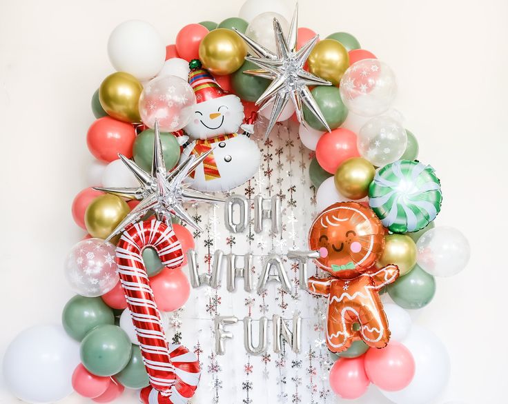 a christmas wreath made out of balloons and other holiday decorations is displayed in front of a white wall