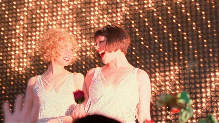 two women standing next to each other in front of a wall with lights on it