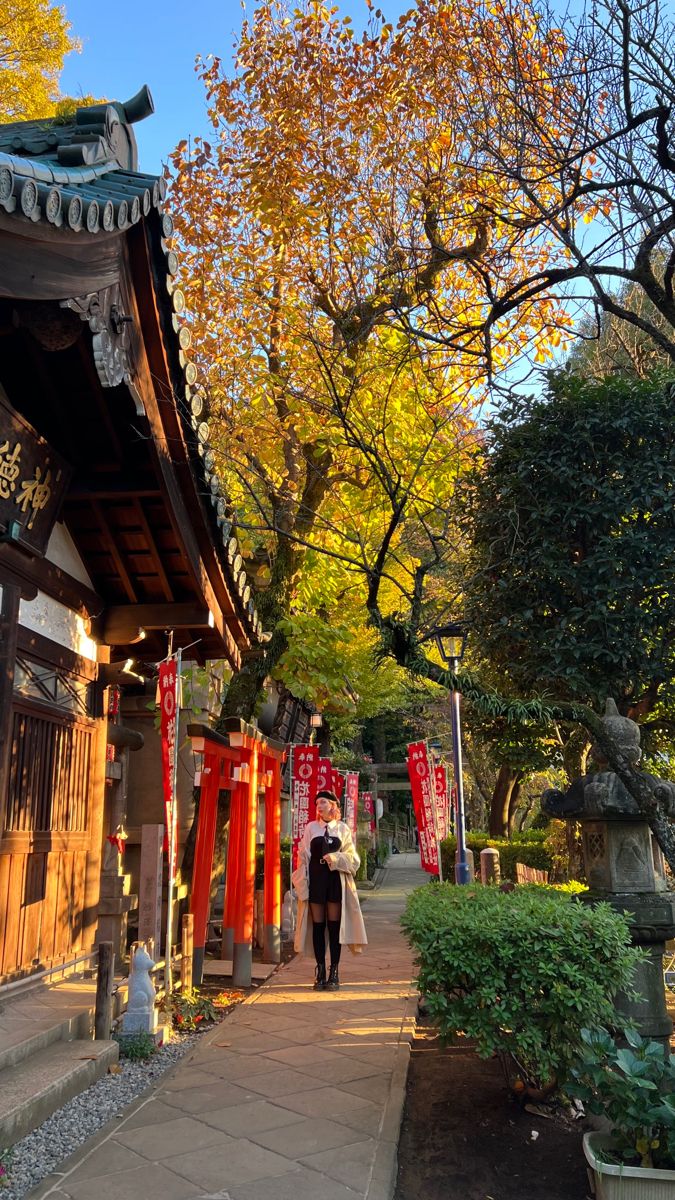 a woman walking down a path in front of a building with red lanterns hanging from it's roof