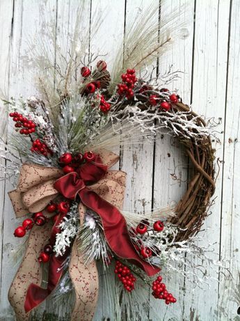 a wreath with red berries and white flowers on it is hanging against a wooden wall