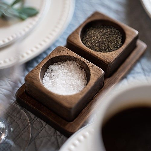 two wooden bowls filled with sea salt on top of a table next to cups and saucers