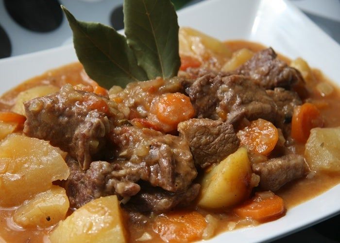 a white plate topped with meat and potatoes covered in gravy next to a leaf