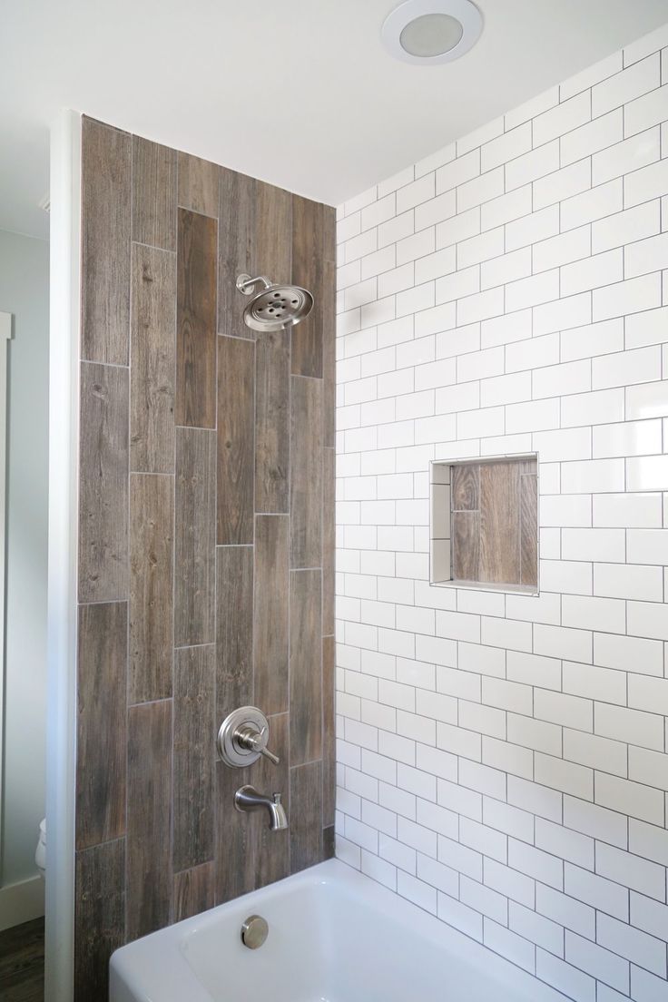 a white tub sitting next to a wooden wall in a bathroom with tile on the walls