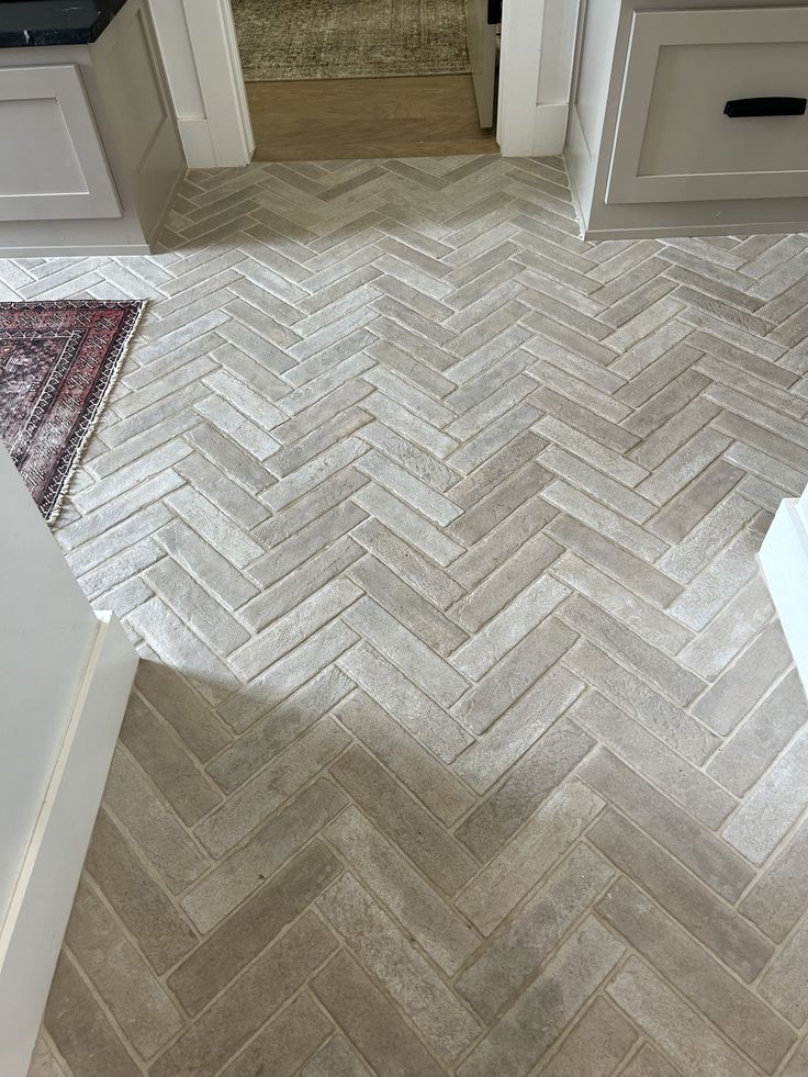 a kitchen floor with white cabinets and gray herringbone tile