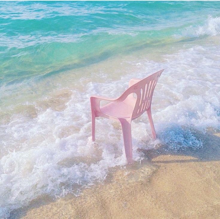 a pink plastic chair sitting on top of a sandy beach next to the ocean water