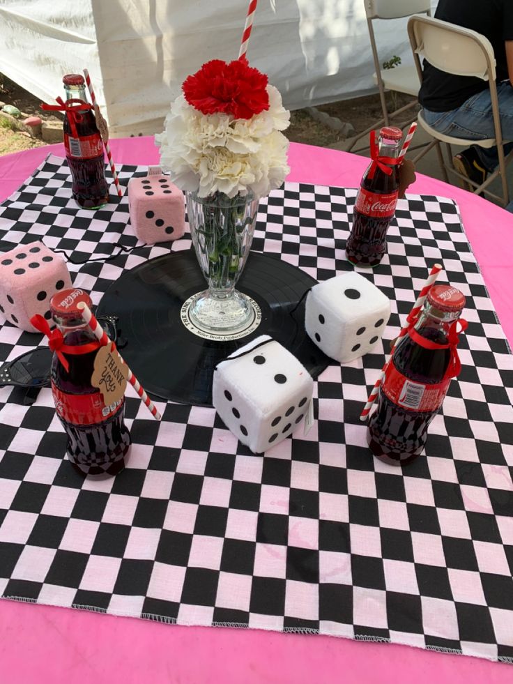 a table topped with dice and flowers on top of a black and white checkered table cloth