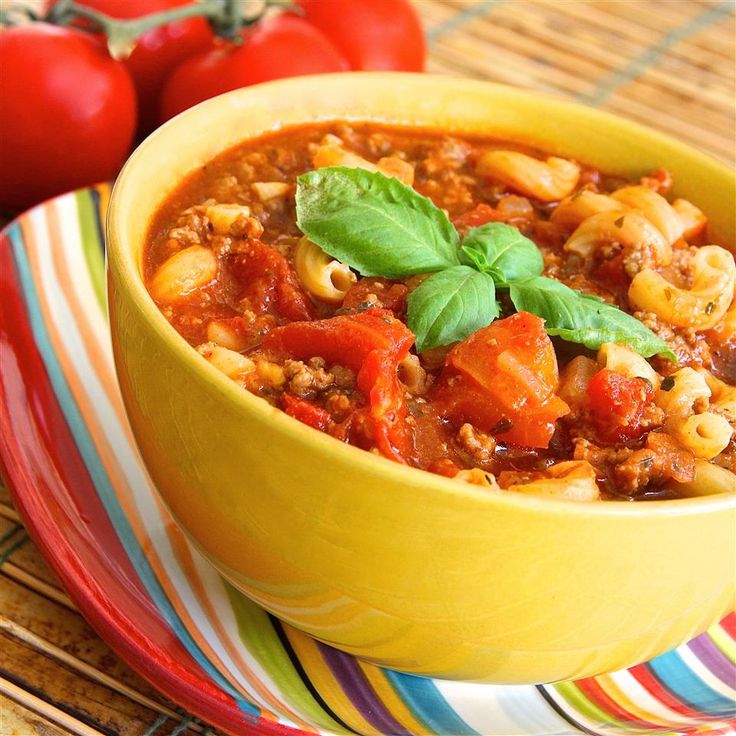 a yellow bowl filled with pasta and vegetables on top of a colorful plate next to tomatoes