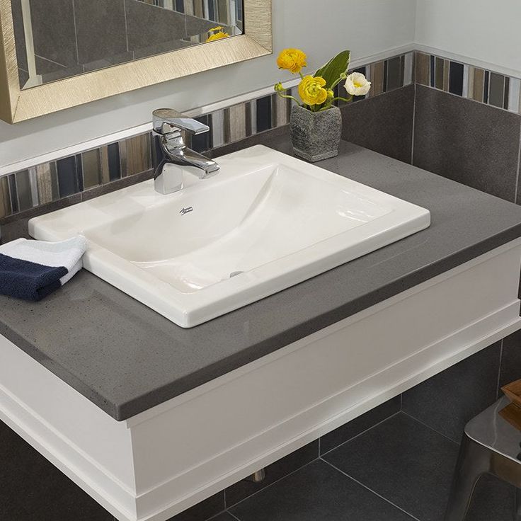 a white sink sitting on top of a counter next to a mirror and yellow flowers