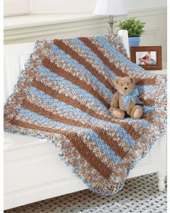 a teddy bear sitting on top of a bed under a blue and brown crocheted blanket