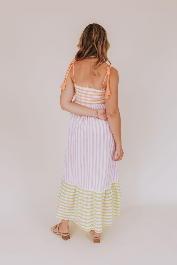 Stay cool and stylish with our Sorbet Splash Dress! The adjustable spaghetti straps with tassels add a playful touch to a smocked bodice for a personalized fit. With a fun multi-colored striped pattern, this dress is perfect for a hot summer day. Say hello to your new favorite outfit! Details Adjustable spaghetti straps with tassels Smocked bodice Multi-colored striped pattern Sizing Approximate measurements: SIZE LENGTH BUST Small 48" 28" Medium 49" 30" Large 50" 32" Fabric has stretch in the b Spring Cotton Dress With Back Tassel Tie-up, Nursing Friendly Tops, Striped V-neck Summer Sundress, Striped V-neck Sundress, Vertical Stripes V-neck Vacation Dresses, Nursing Friendly Dress, Sleeveless Tie-dye Spring Dress, Plus Jumpsuit, Tank Top Long Sleeve