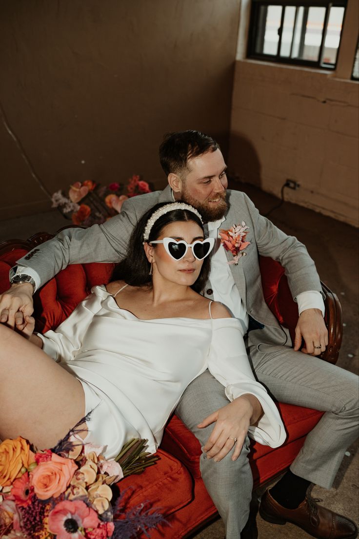 a man and woman are sitting on a red chair with flowers in their lapels