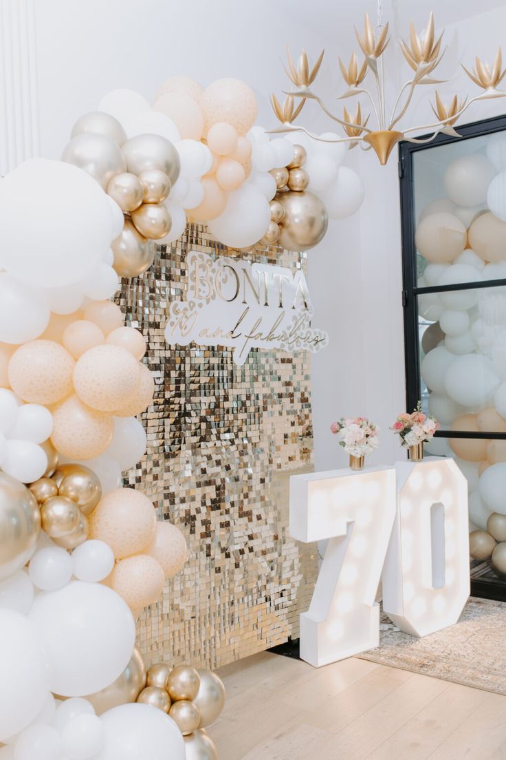 the balloon arch is decorated with gold, white and silver balloons for an 70th birthday party