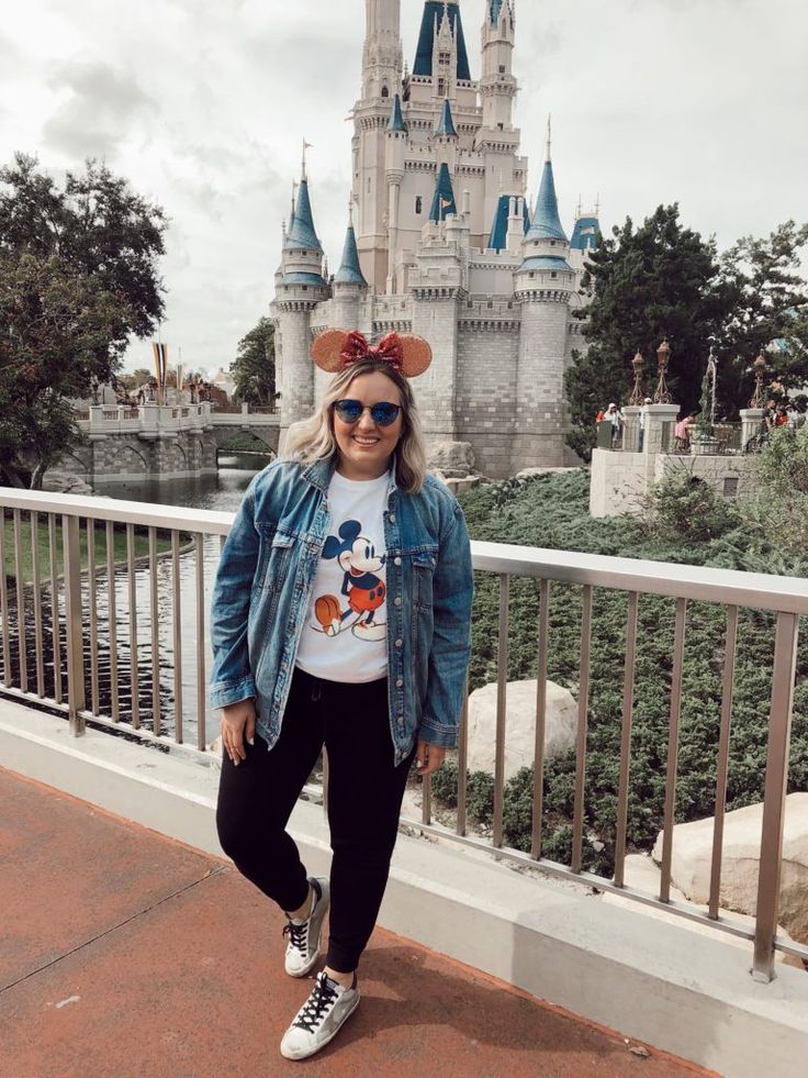 a woman standing in front of a castle wearing minnie mouse ears and mickey mouse t - shirt