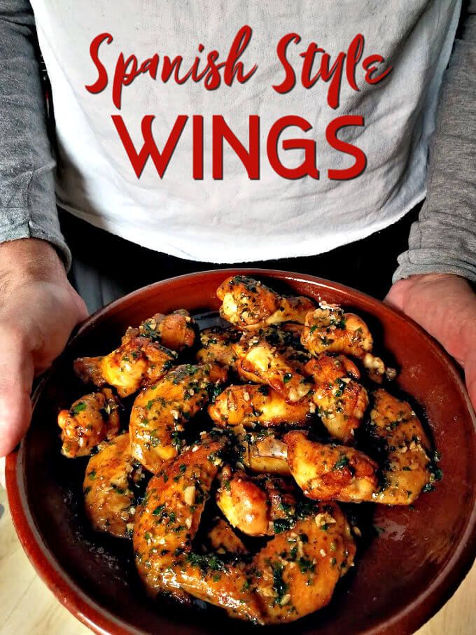 a person is holding a bowl full of shrimp and wine wings with the words spanish style wings above it