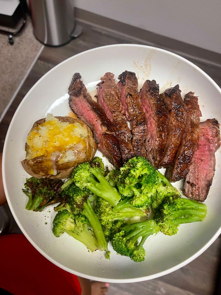 a white plate topped with steak and broccoli next to a potato on top of a counter