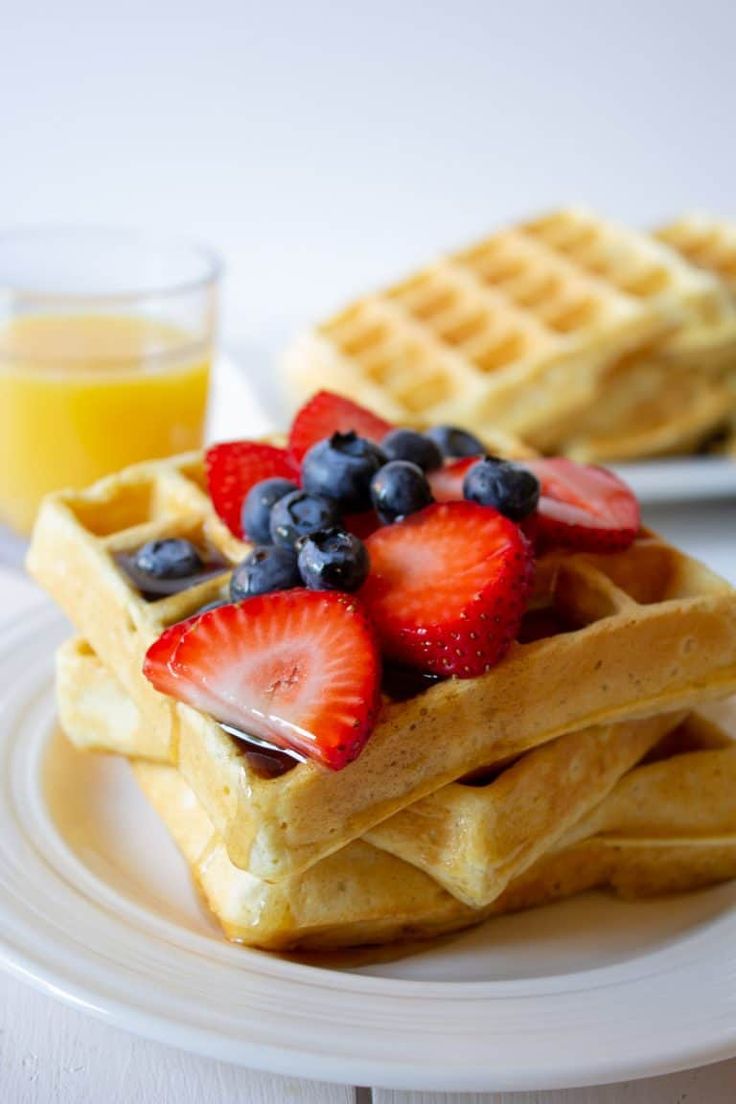 a stack of waffles topped with fruit on top of a white plate next to a glass of orange juice