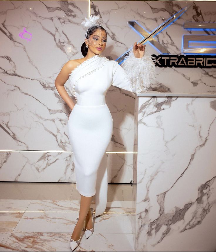 a woman in a white dress standing next to a marble wall with scissors on it