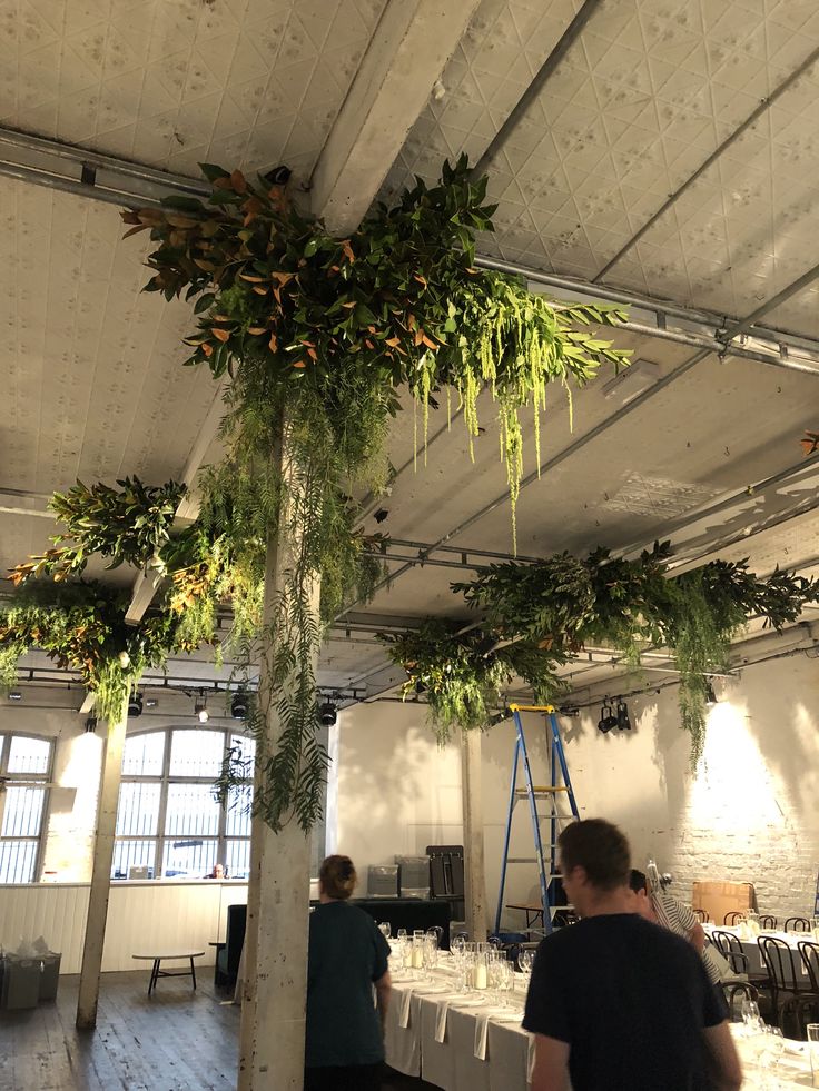 people are standing around tables with plants hanging from the ceiling