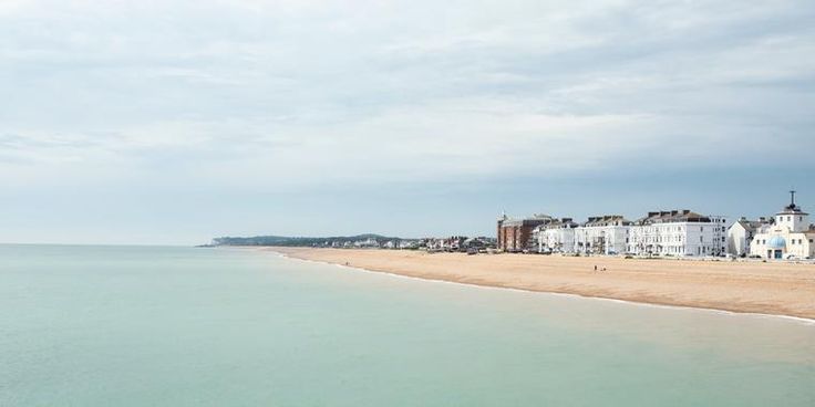 a beach with houses on the shore and water in the foreground, under a cloudy sky