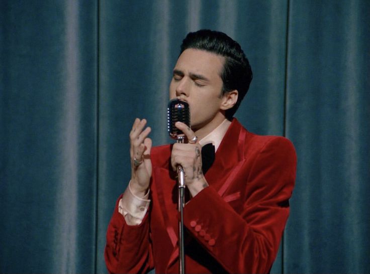 a man in a red suit is holding a microphone and singing into the microphone with his hands