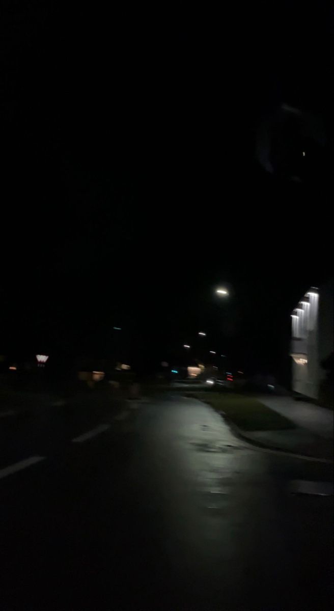 an empty street at night with the lights on and no one in the dark is seen