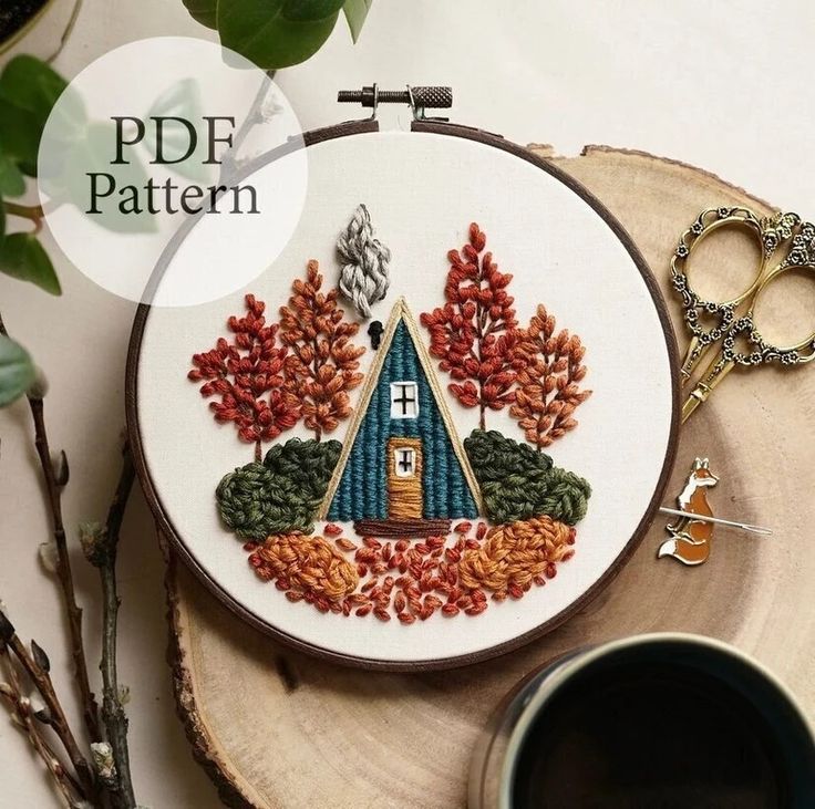 a cross stitch pattern with a house in the woods on it and a cup of coffee next to it