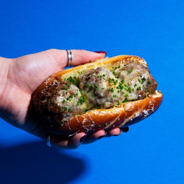 a hand holding a meatball sub sandwich on a bun with cheese and chives