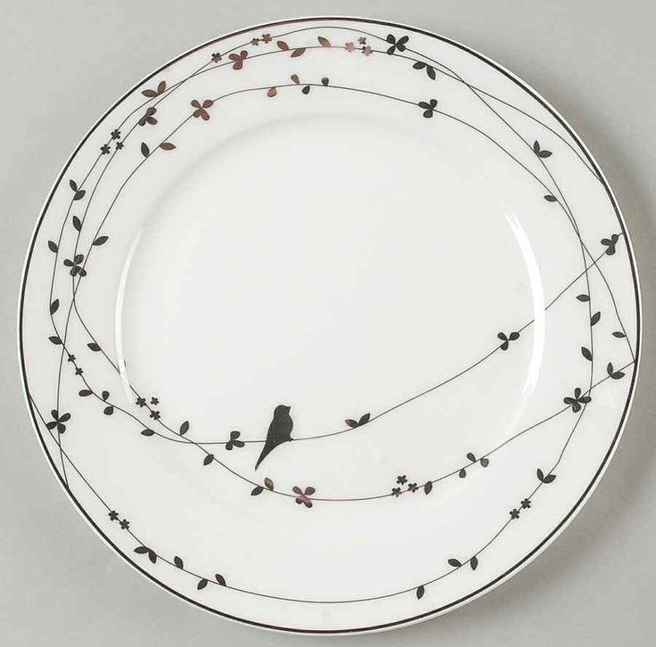 a white plate with black birds on the rim and branches in the middle, against a gray background