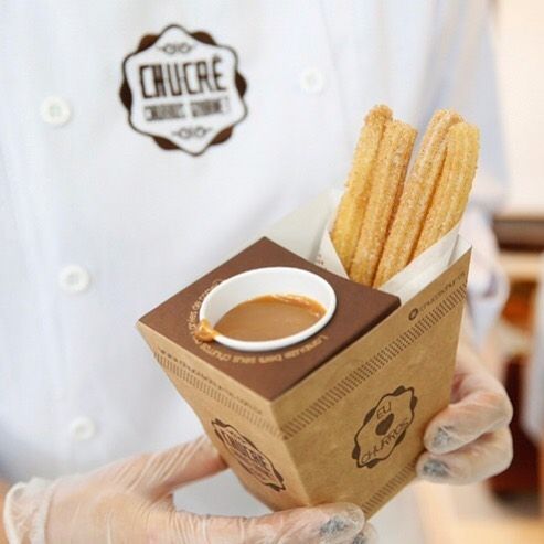 a person in white gloves holding a box with some food inside of it and dipping sauce on top