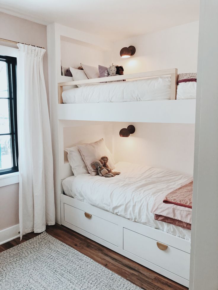 bunk beds with white linens and pillows in a small room next to a window