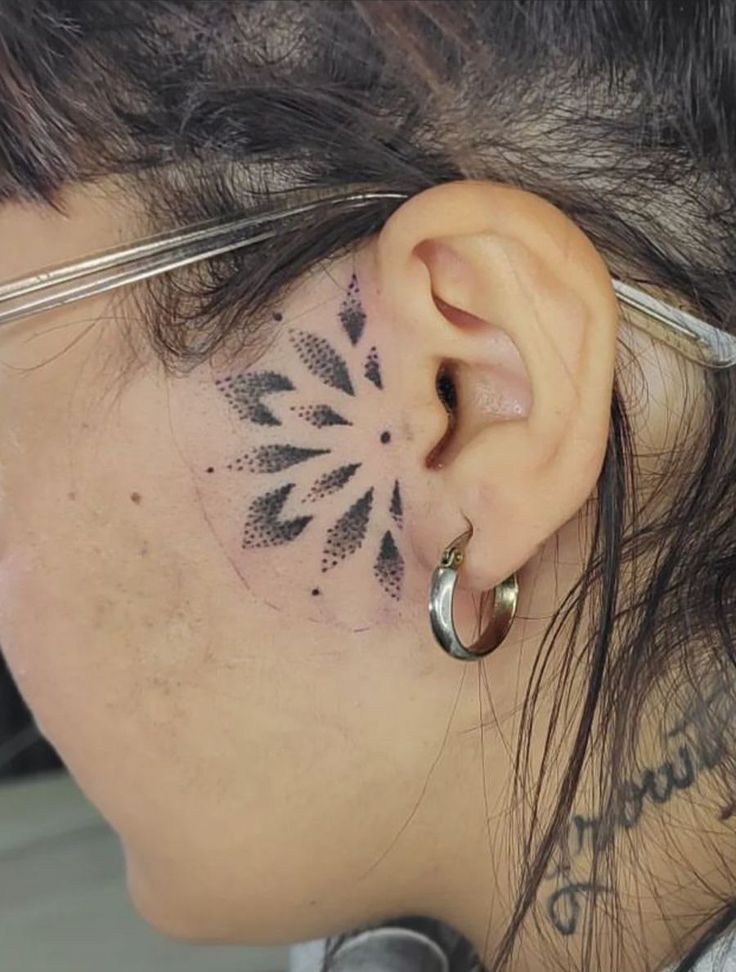 a woman has a tattoo on her ear and behind her ear is a circular flower